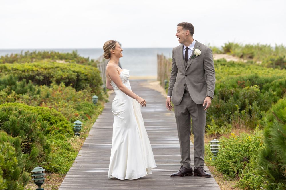Bride and groom holding hands on a coastal boardwalk surrounded by lush seaside greenery.