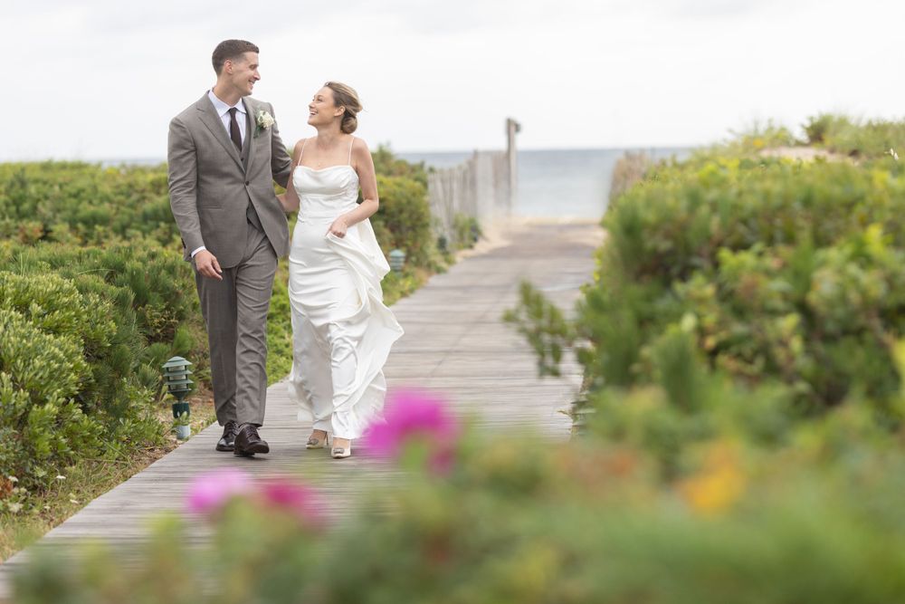 Happy couple walking on a beach boardwalk, bride in white gown, groom in grey suit.