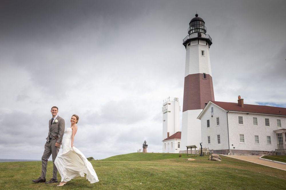 Wedding couple posing in front of historic Montauk Lighthouse on a dramatic cloudy day.