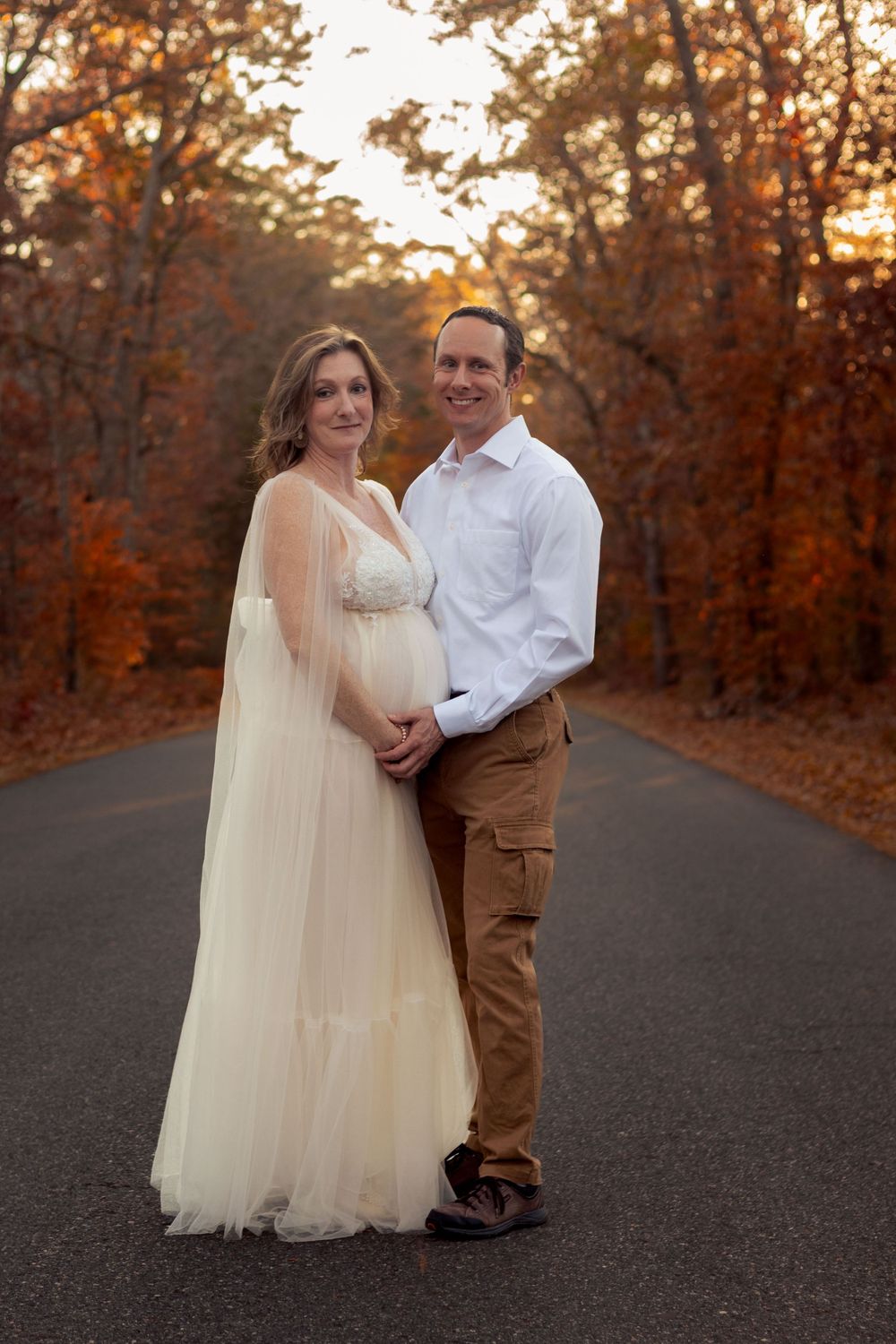 A man and woman pose in the road with fall colors around them.