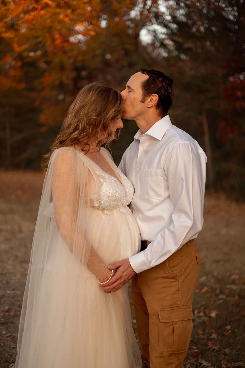 A man kisses the forehead of his partner and holds her baby belly.