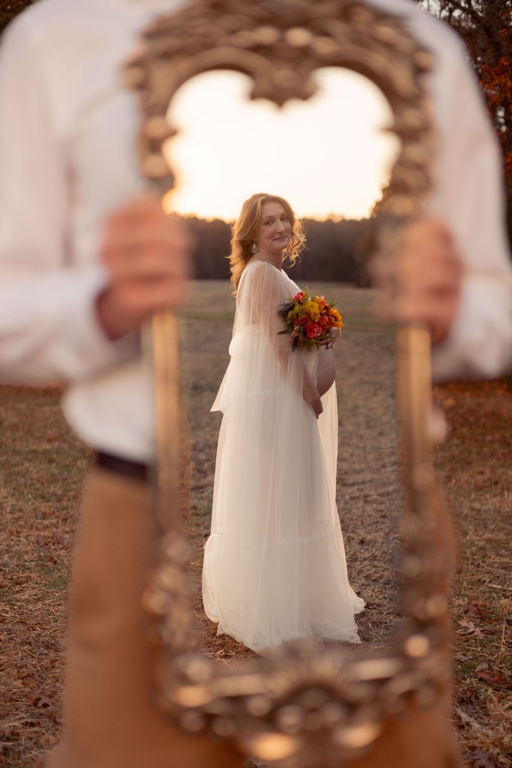 A man holds a mirror, the reflection is a pregnant woman holding a bouquet.