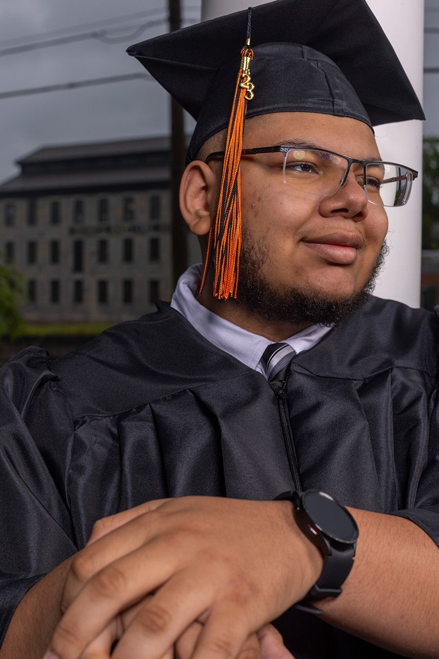 Graduate in cap and gown with orange tassel wearing glasses.