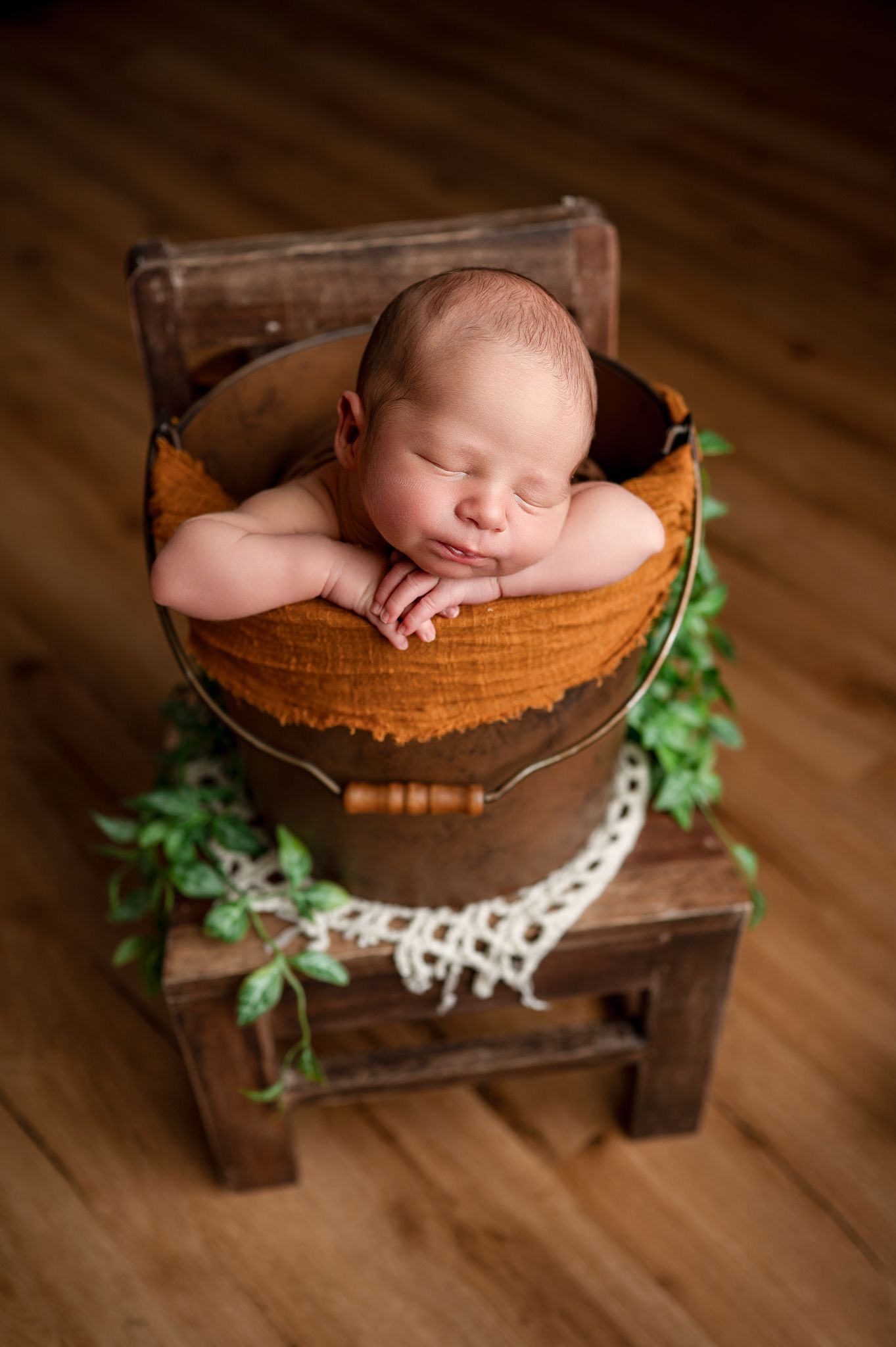 Sleeping baby rests peacefully on green fabric in rustic woven basket during newborn photography session.