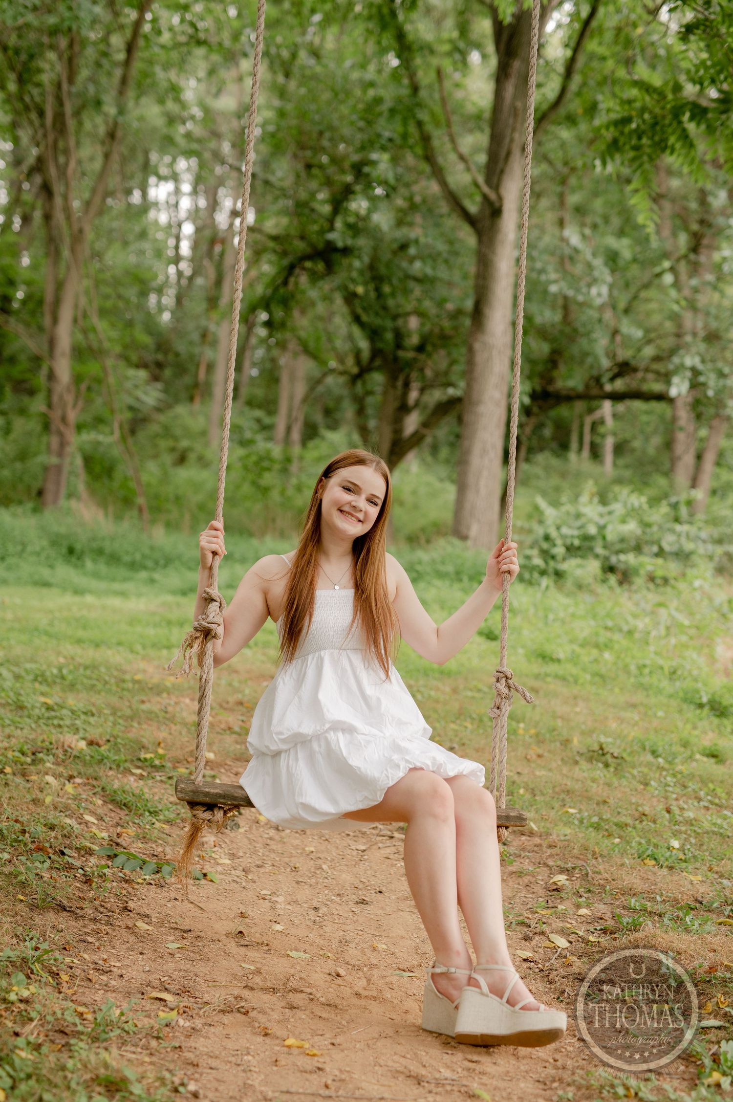 Graduate enjoying moment on rustic rope swing in wooded area.
