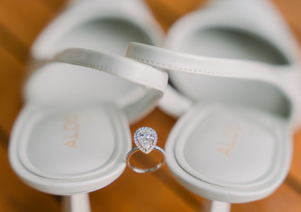 Diamond engagement ring positioned between a pair of white slippers on a wooden surface.