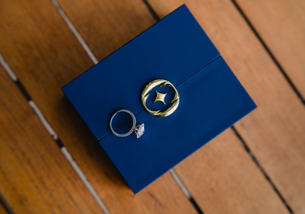 Wedding rings displayed on dark blue velvet box against wooden surface.