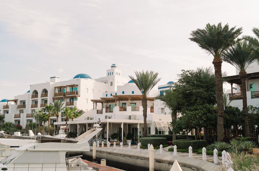 Mediterranean-style resort with white architecture and palm trees along a waterfront walkway.