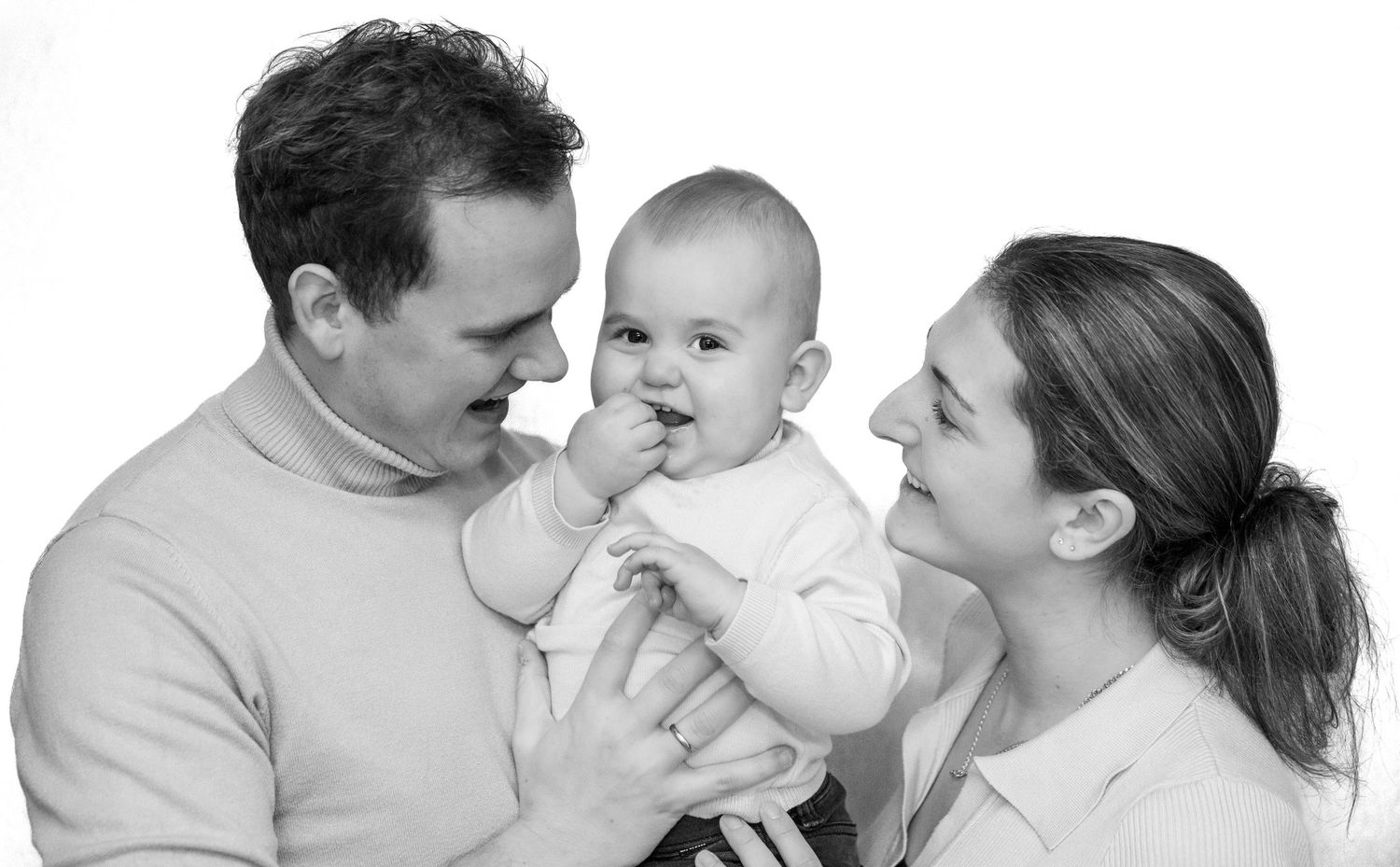 Zwart-wit portret van lachende ouders die een blije babyjongen vasthouden tegen een witte achtergrond.