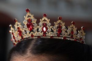 Gold tiara with red ruby gemstones and crystal accents worn on dark hair.