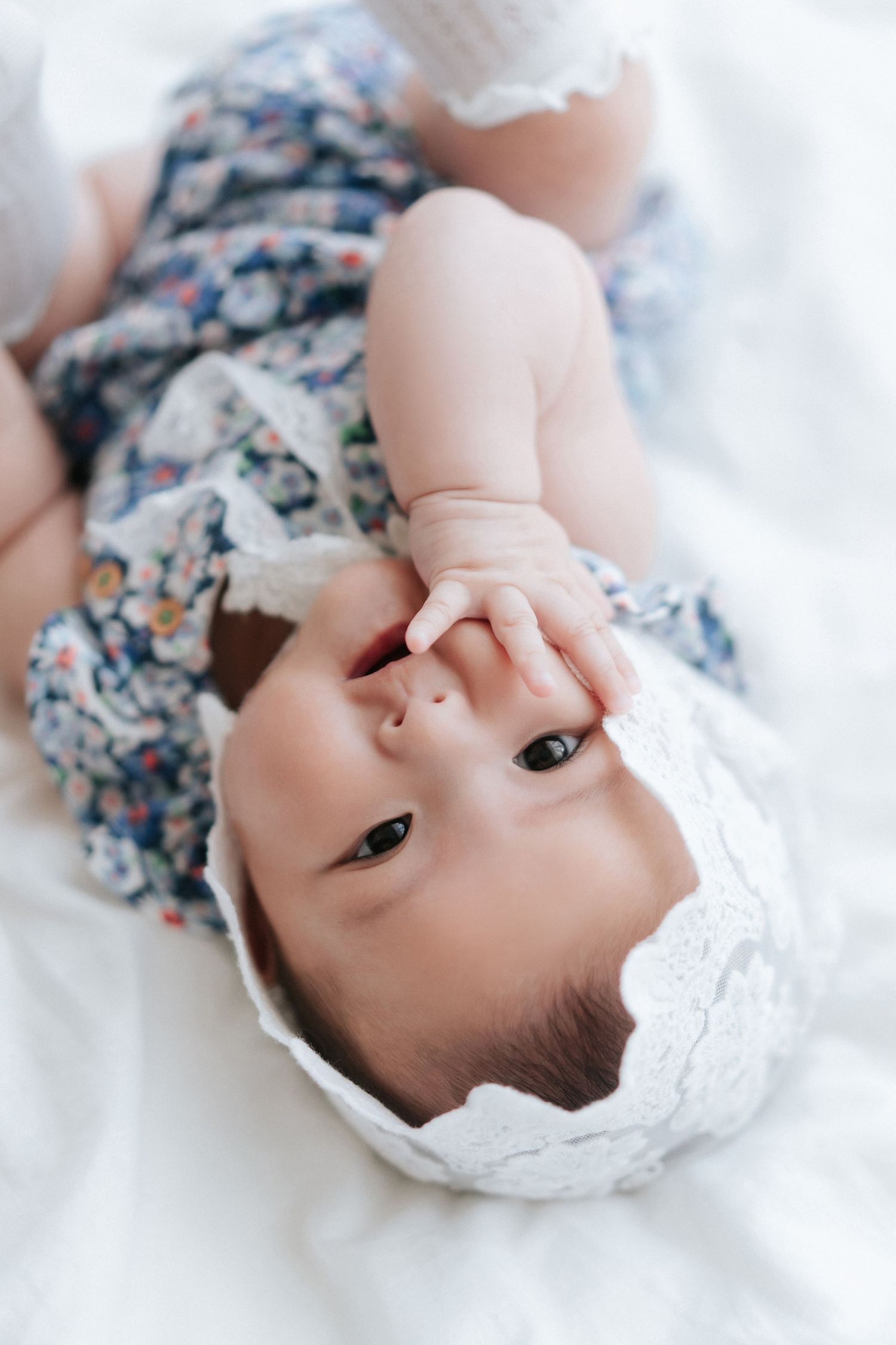 A newborn baby wearing white lace clothing smiles while lying on soft beige fabric during a professional photo session身穿白色蕾絲衣服的新生兒躺在柔軟的米色布料上