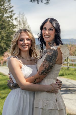 Two smiling women with tattoos hugging outdoors in white dresses on a sunny day in eatonville wa taken by roy wa photographer