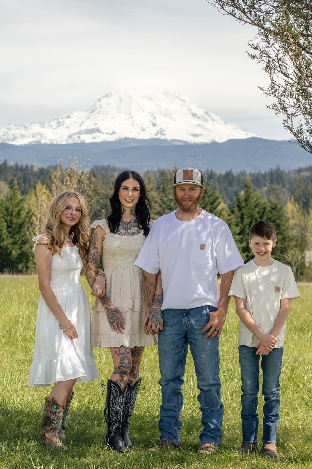 Family of four posing together in a green field with a snow-capped Mount Rainier in the background taken by washington photographer