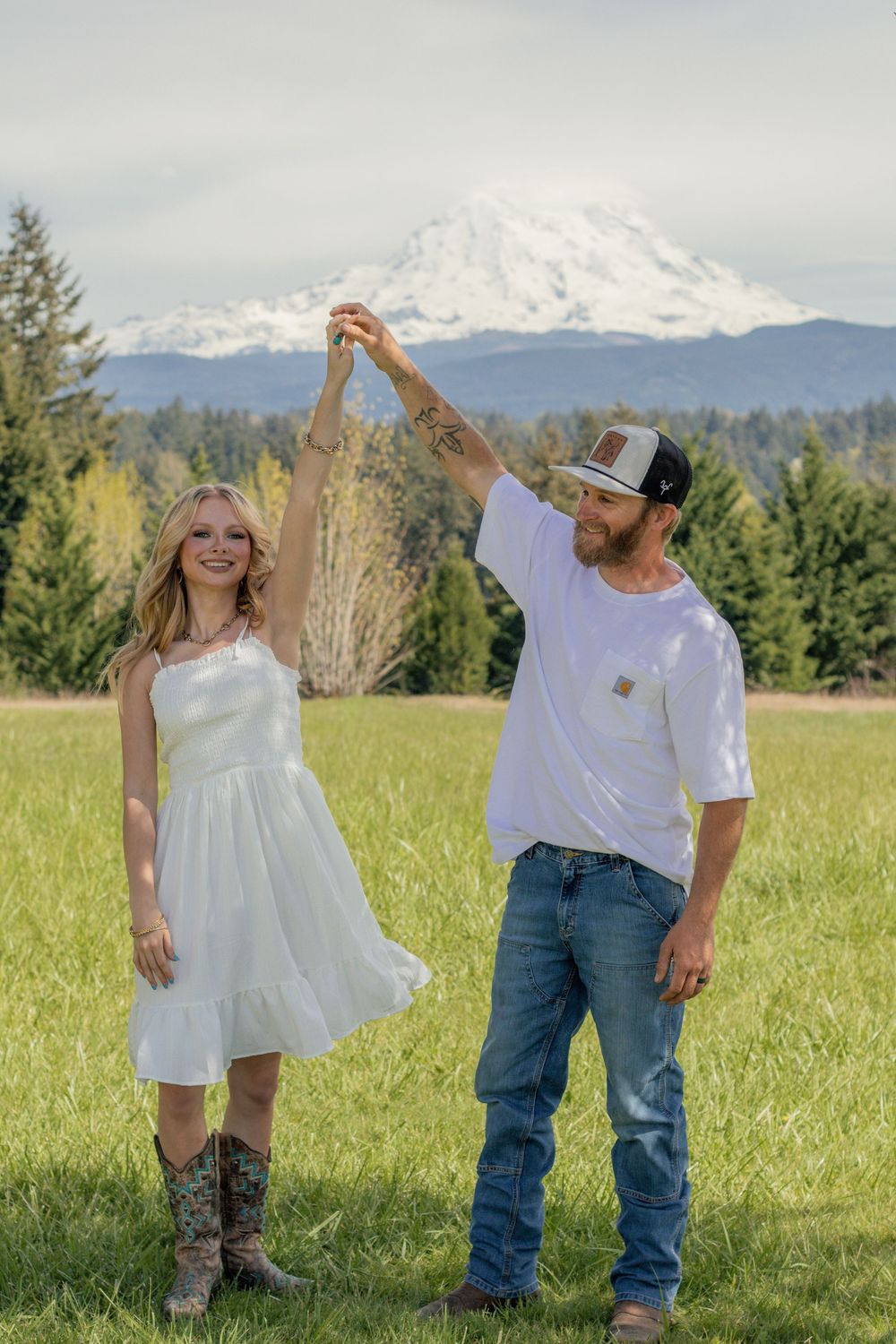 A smiling blonde girl in white dress dancing with a man in a field near eatonville with Mount Rainier behind them taken by roy photographer