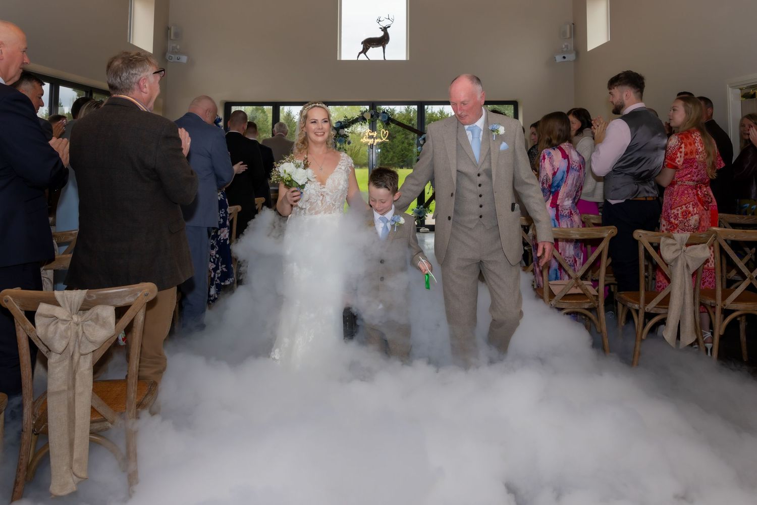 Bride and groom walk down the aisle through dramatic fog effect at elegant wedding venue ceremony. Casual Captures Wedding The Hidden Oak