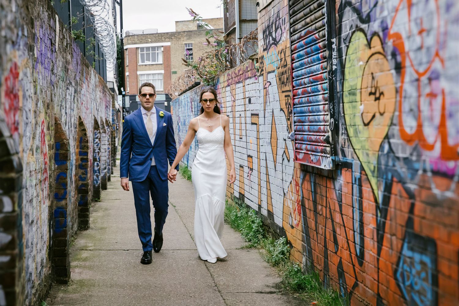 Bride and groom walking hand-in-hand down a graffiti-lined alley in an urban wedding photo.