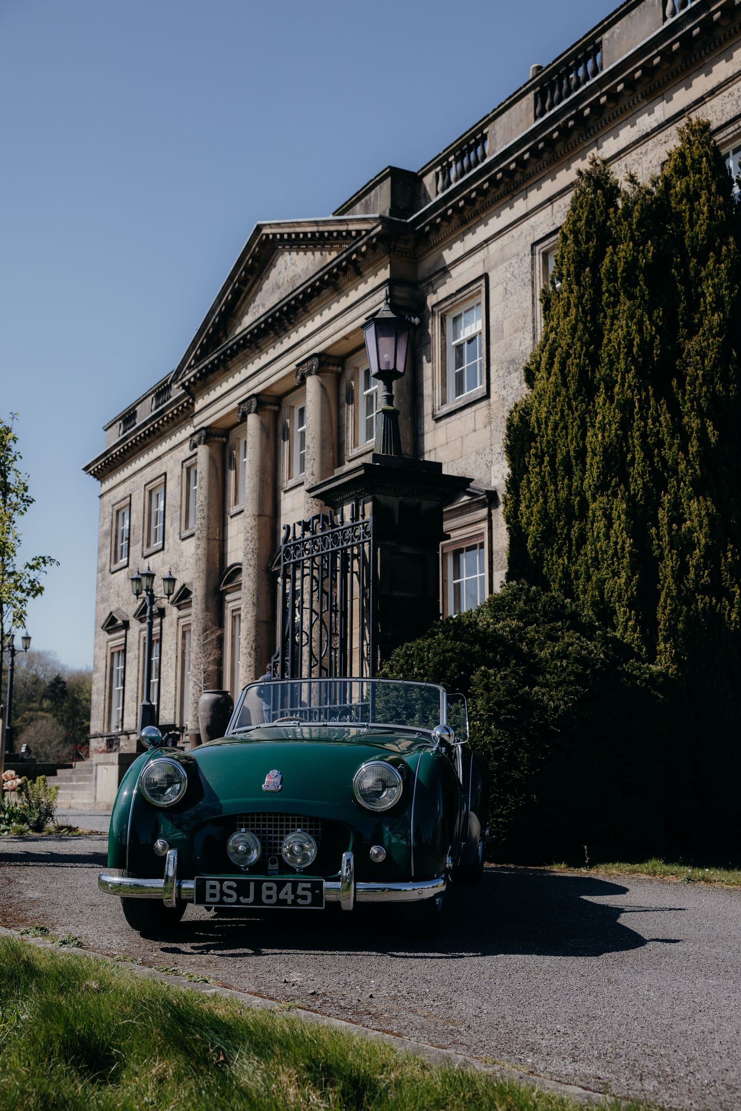 Vintage green Triumph TR3 convertible parked outside a grand Georgian country house on a sunny day. Denton Hall, Yorkshire