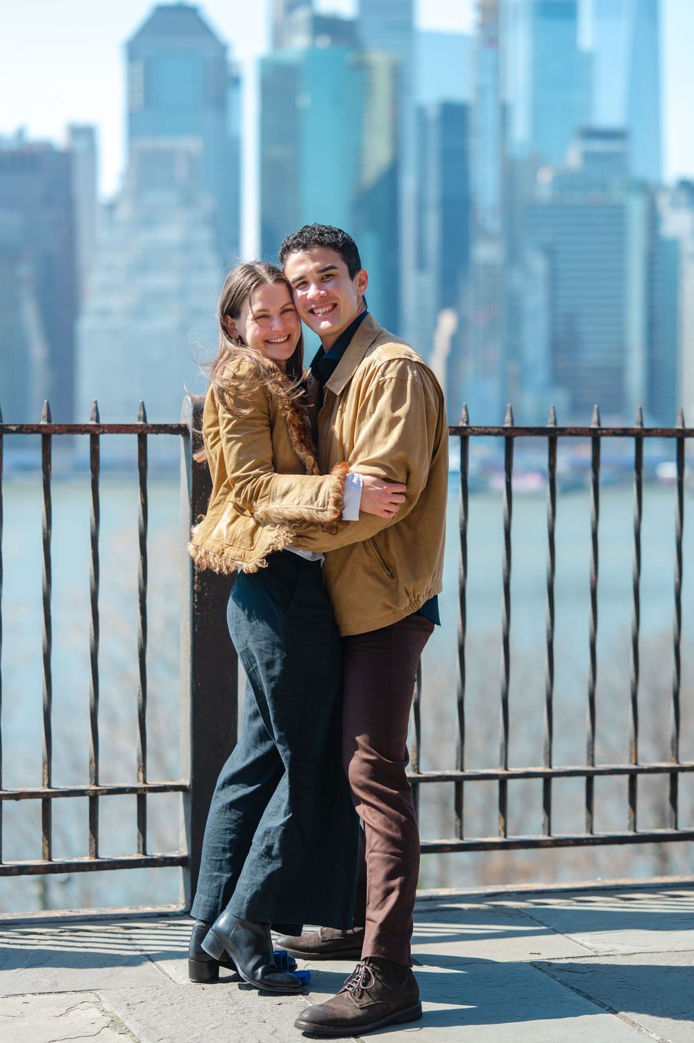 Happy couple embracing and smiling in front of NYC skyline on a sunny day.