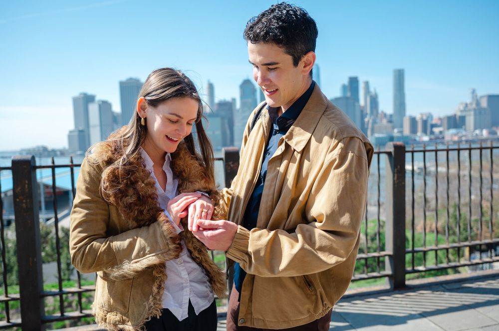 Couple looking at an engagement ring together with the New York City skyline visible behind them.