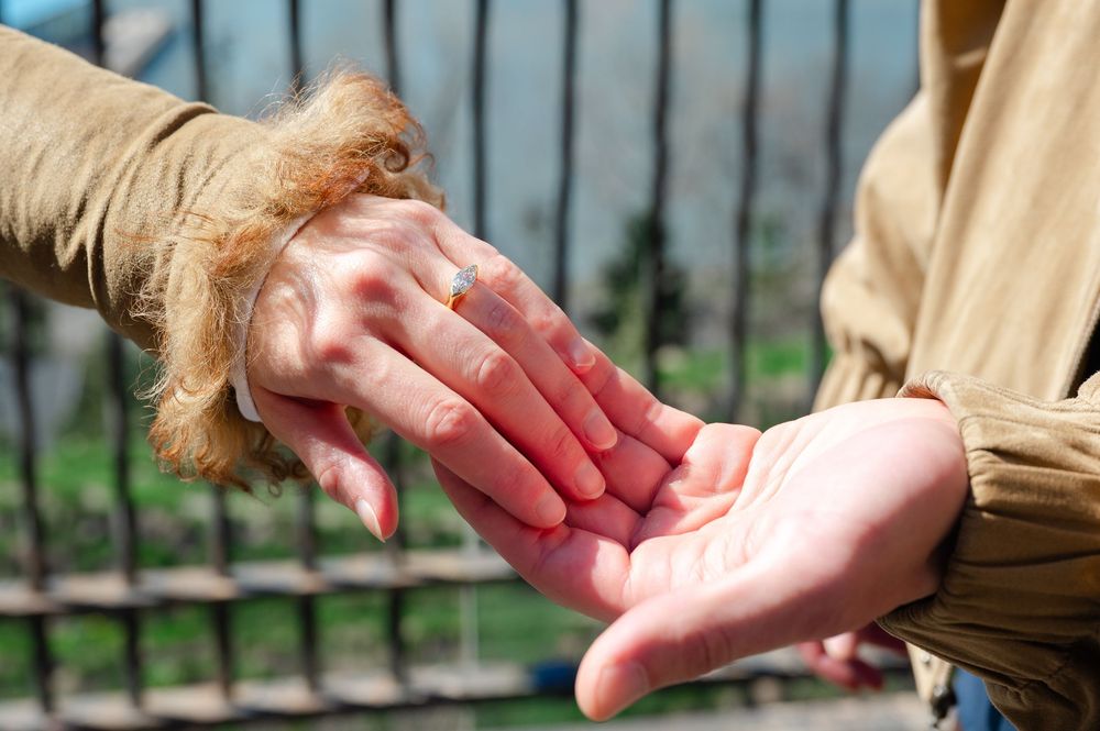 Close-up of engagement ring being placed on woman's finger outdoors in sunlight.