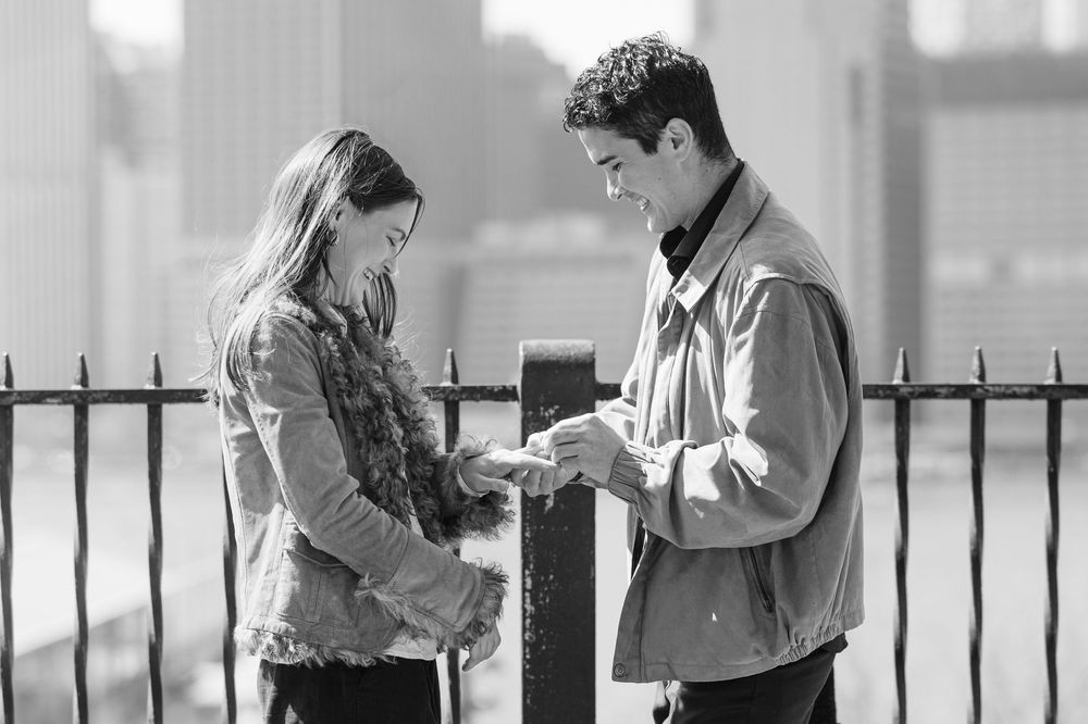 Black and white photo of a young couple sharing a moment by an iron fence outdoors.