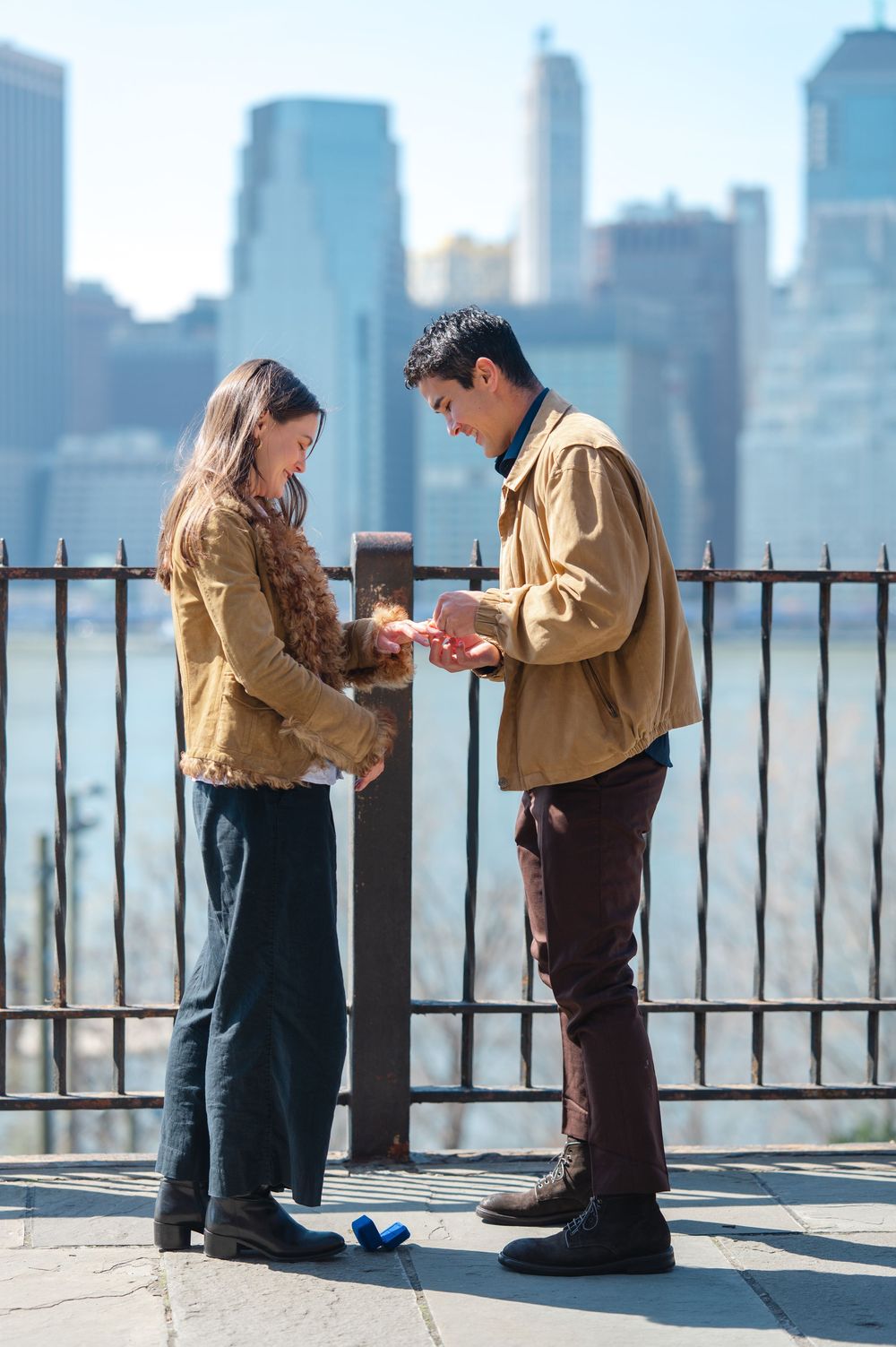Couple examining engagement ring together with Manhattan skyline behind them.