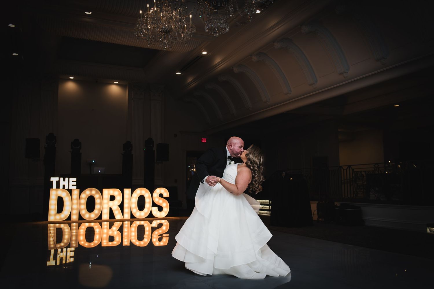 Bride and groom share first dance in elegant ballroom with illuminated THE DIORIOS marquee letters at wedding reception.