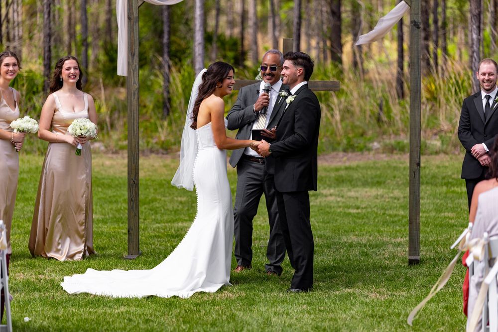 Couple exchanging vows at outdoor wedding ceremony with officiant and wedding party.