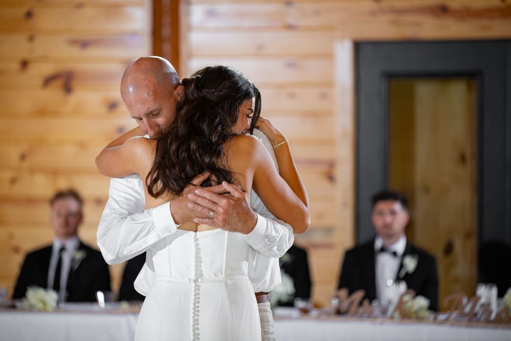 Bride and groom share an emotional first dance hug in a warmly lit wedding reception venue.