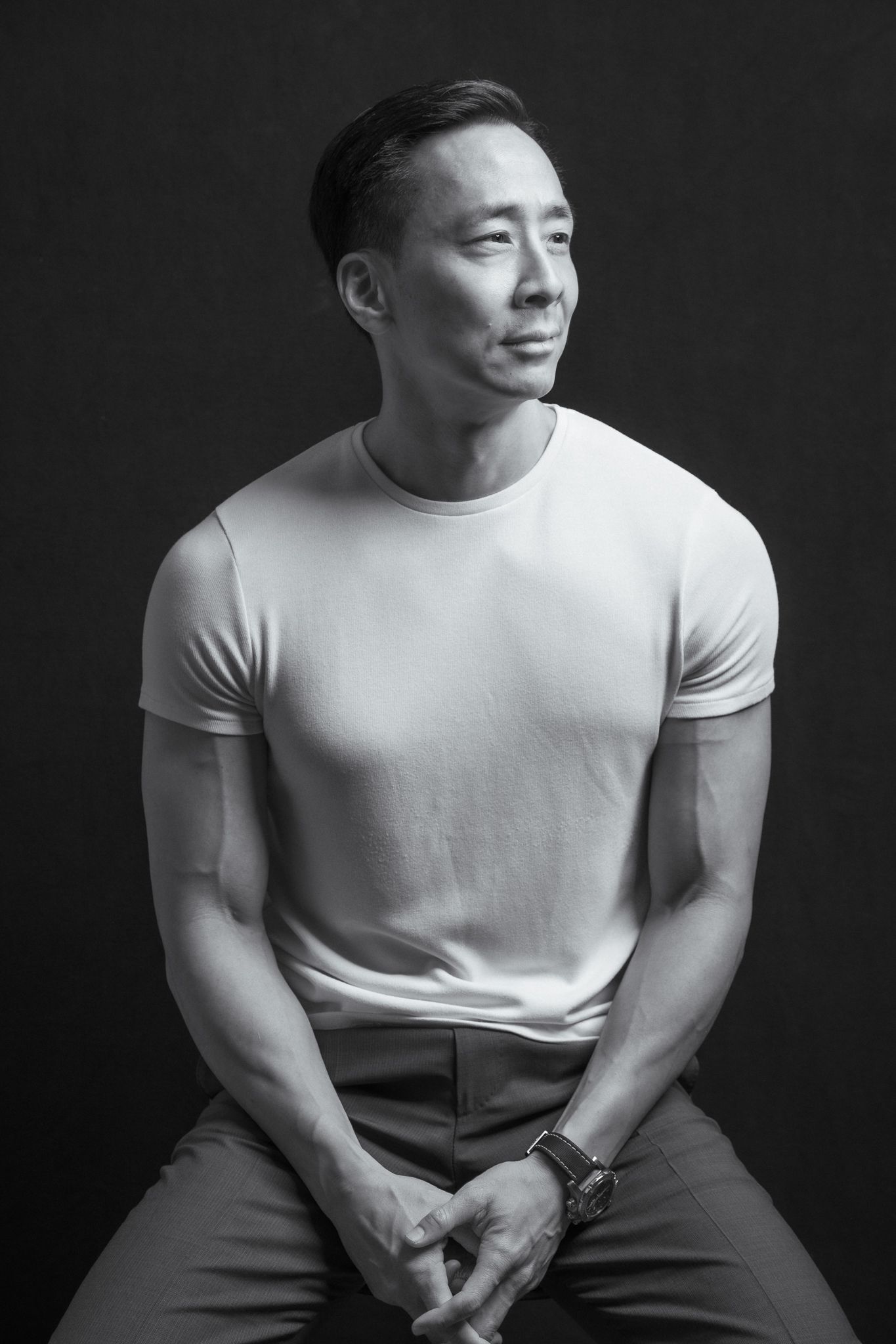 Black and white portrait of athletic man in white t-shirt seated looking away from camera.