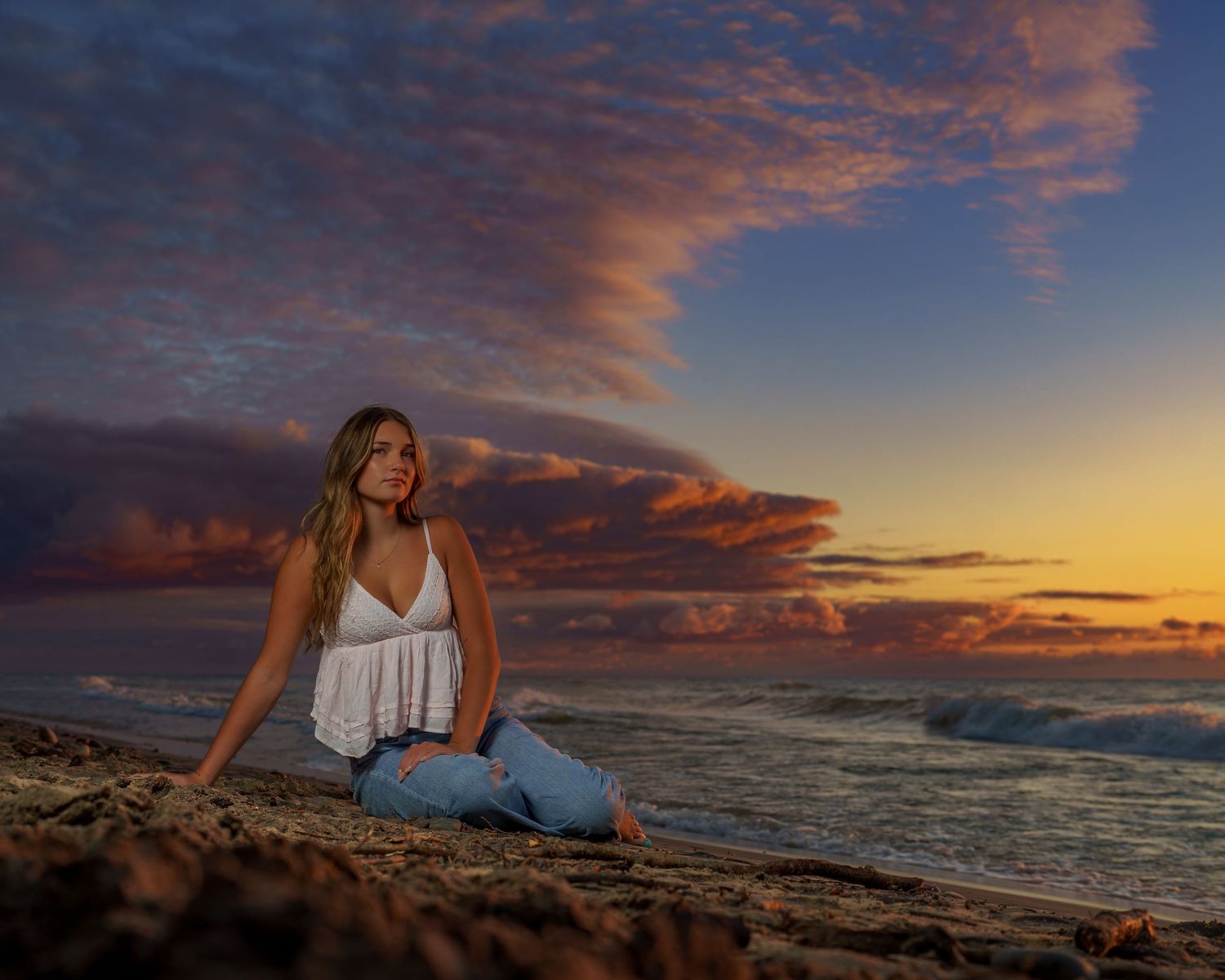 A barefoot teenage boy in white shirt and khaki pants stands on a reflective beach at sunset.