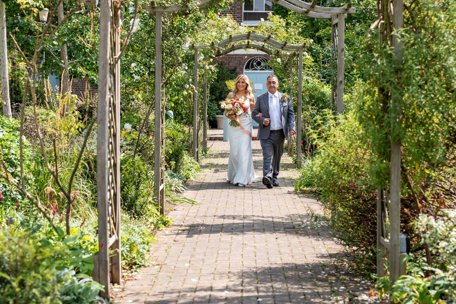 Bride and groom walking through a lush garden archway on their wedding day.