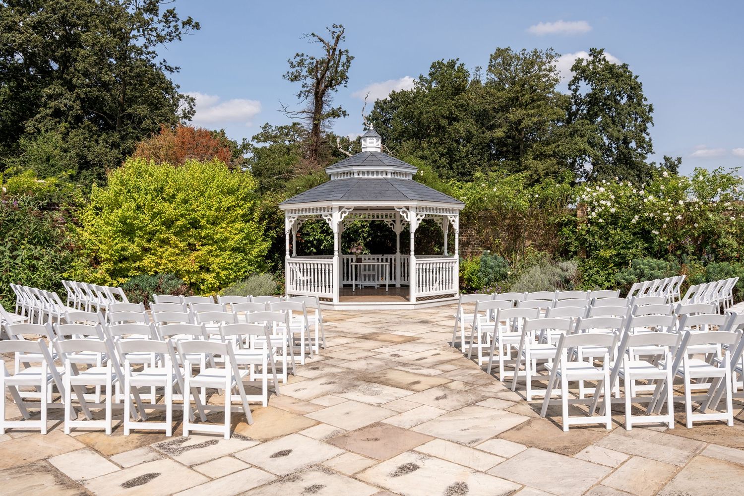 White chairs arranged in rows facing a elegant gazebo in a lush garden, set up for an outdoor wedding ceremony.