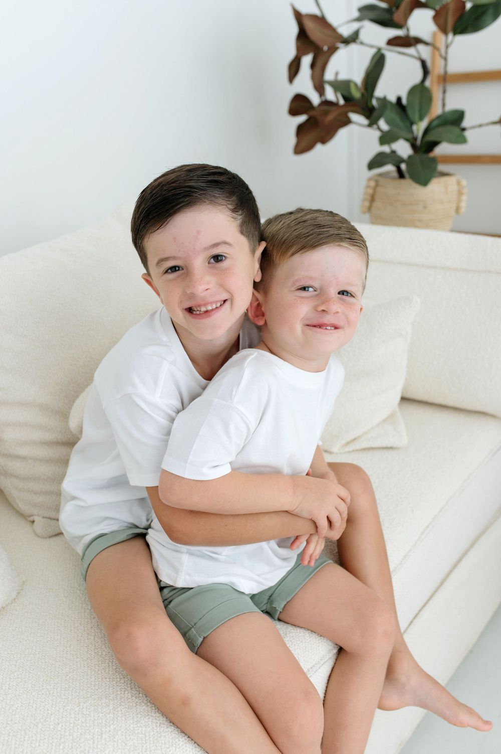 Two happy brothers in matching white shirts embrace on a couch.