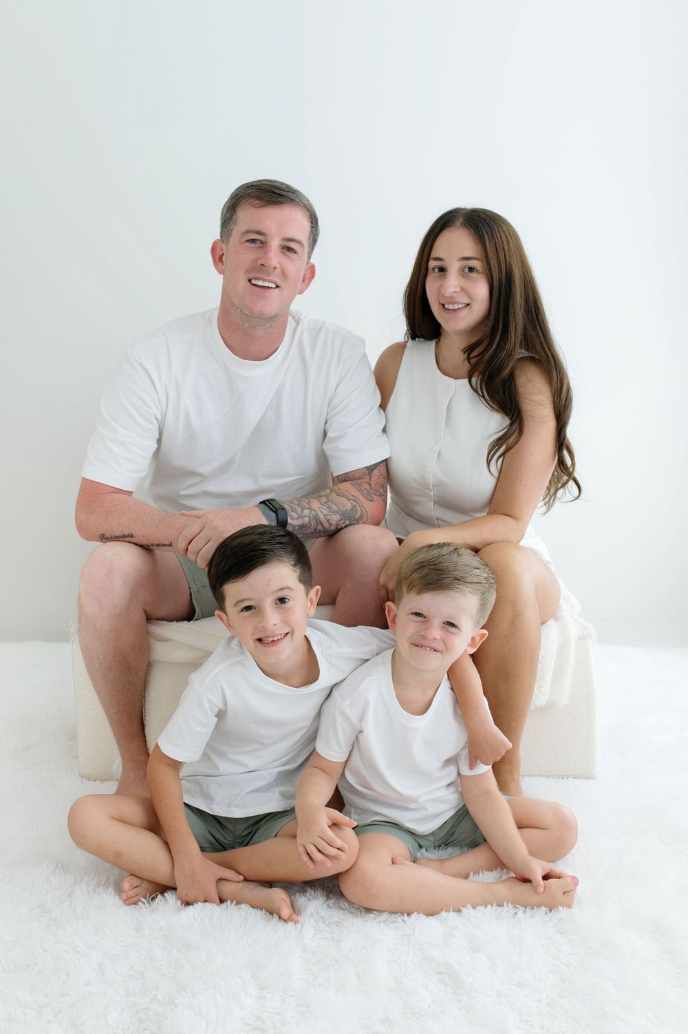 Smiling family of four in white outfits pose together at home.