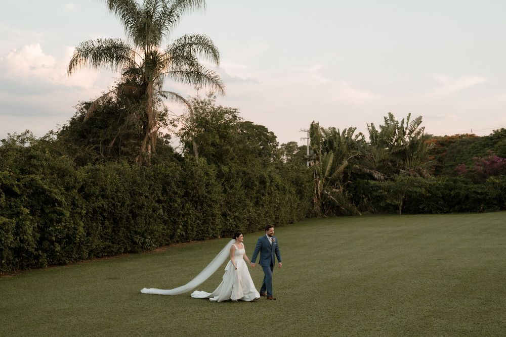 Romantic wedding couple poses in a lush green field at sunset with palm trees in the background.