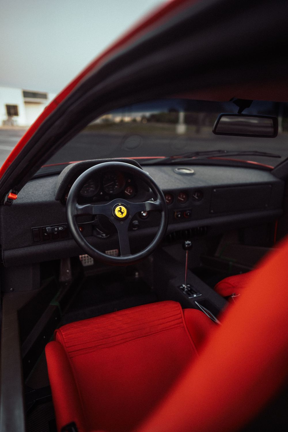 Ferrari sports car interior with red leather seats, black dashboard, and iconic prancing horse steering wheel emblem.