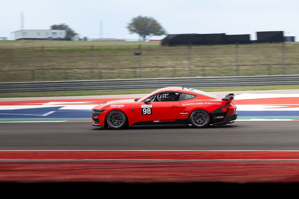 Red Ford Mustang race car number 98 speeding on a professional racing circuit track during a motorsport competition.