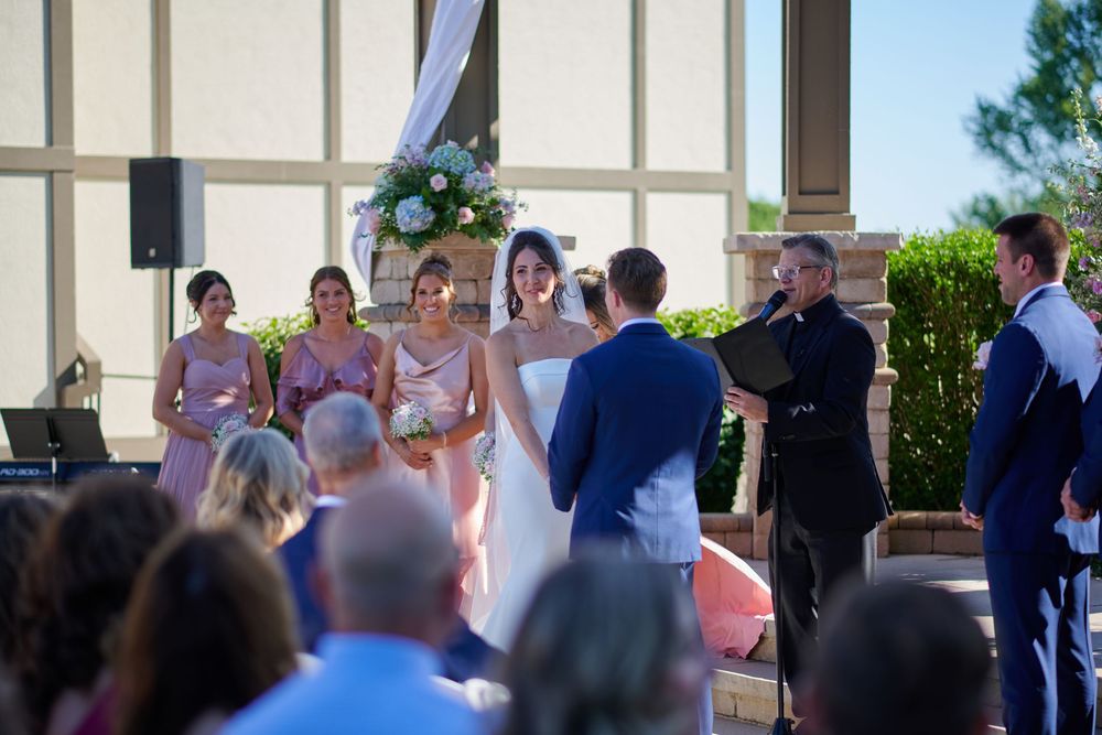 Outdoor wedding ceremony with bride, groom, officiant, and bridesmaids in pink dresses gathered at the altar.