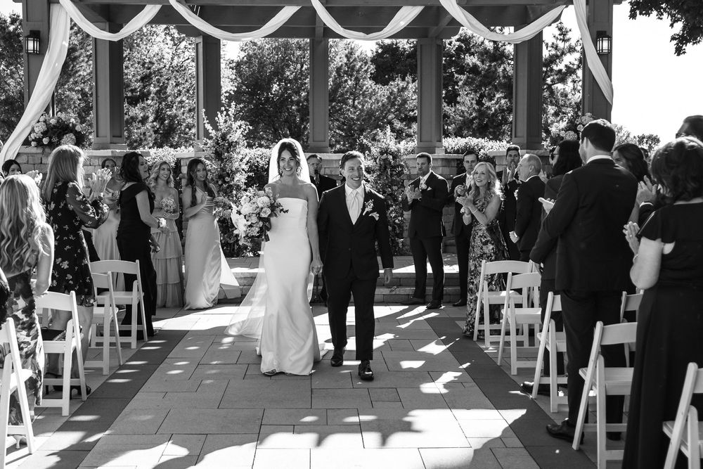 Bride and groom walk down the aisle at an outdoor wedding ceremony in black and white photo.
