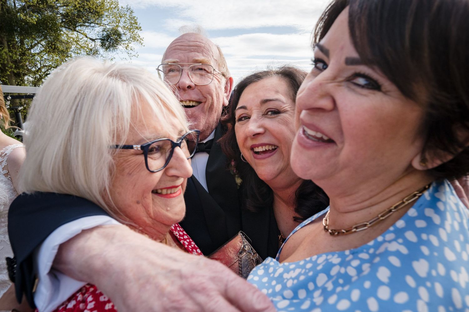 Group of joyful people hugging and smiling at an outdoor celebration or wedding event.