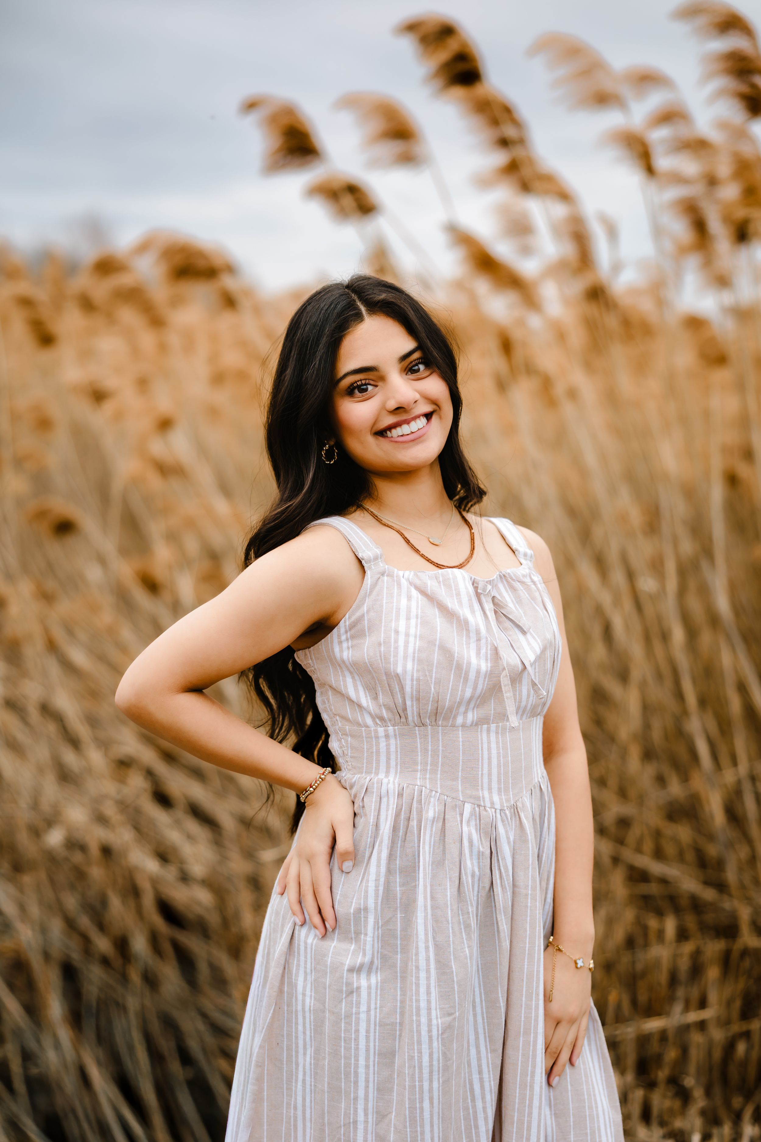 Young woman in striped sundress smiling in a field of tall golden grass.