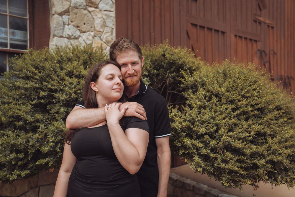 Happy couple embracing outdoors near a rustic barn, woman leaning back against her bearded partner.