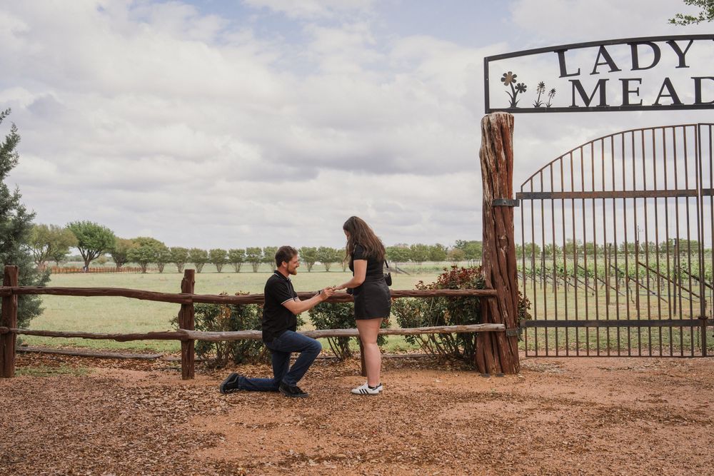 Man proposing on one knee to woman at Lady Meadows ranch gate entrance on a cloudy day.