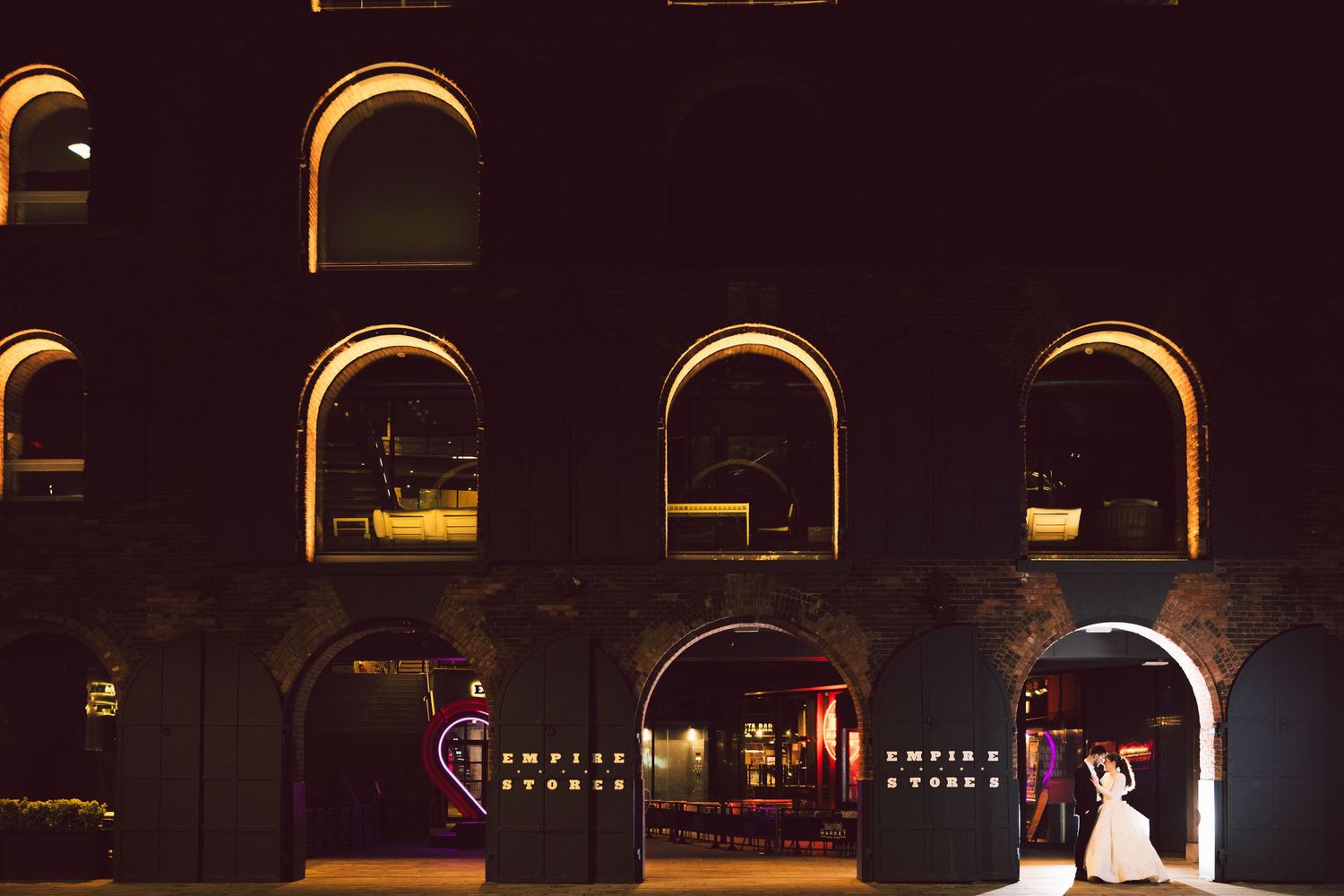 Bride and groom dancing at night outside Empire Events venue with arched windows glowing warmly.