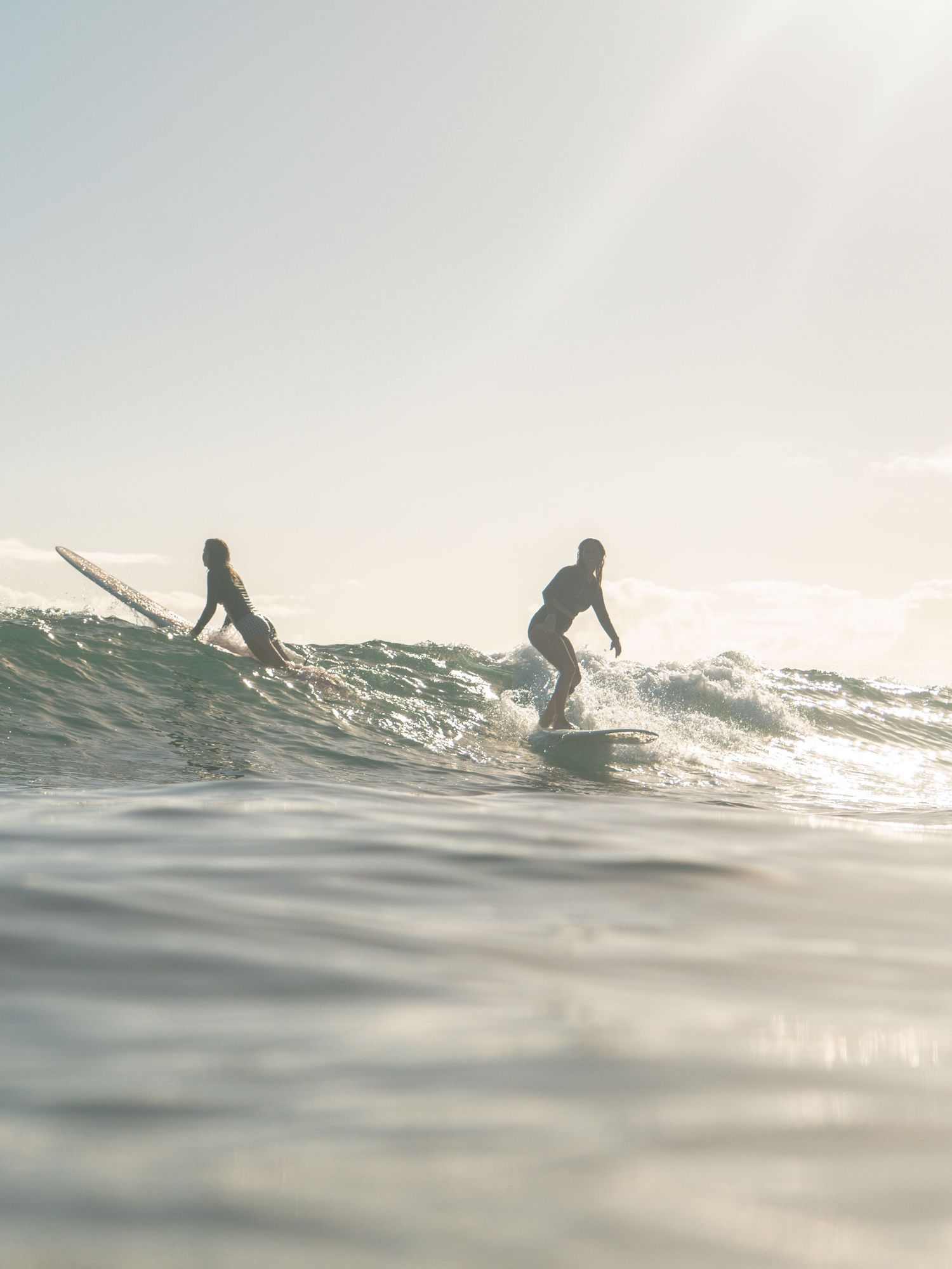 two female surfers on a wave laughing at each other at a point break near Newcastle NSW
