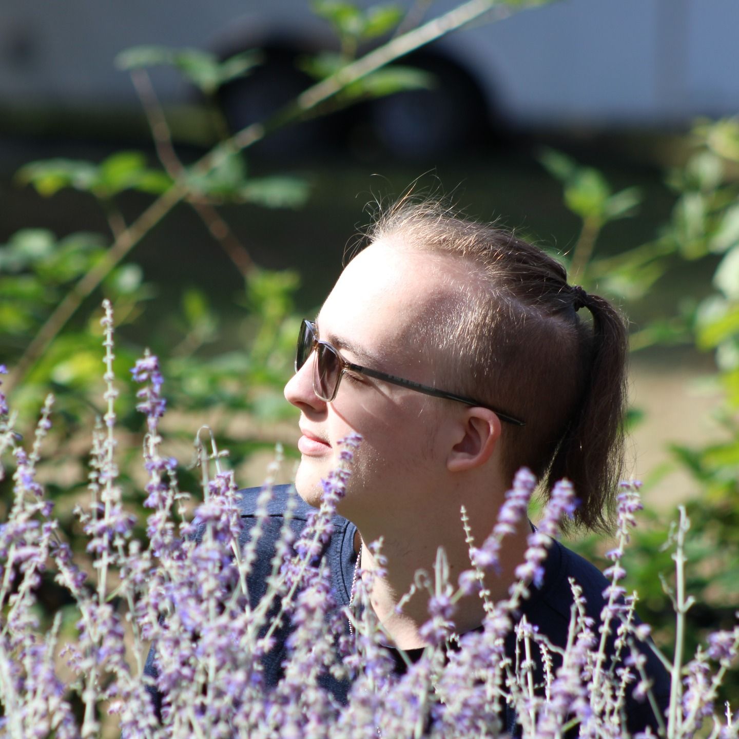 Natural light portrait of a young man smiling outdoors among flowers.