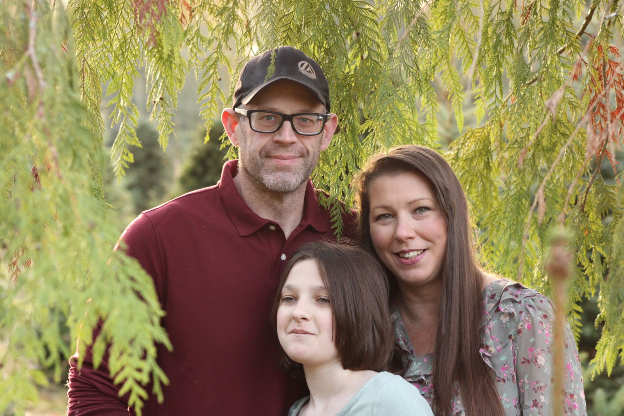 Family standing together under soft greenery during a natural outdoor family photography session