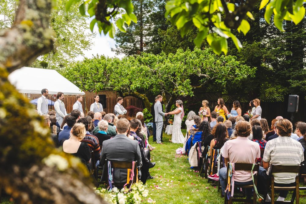 Outdoor wedding ceremony with guests seated on chairs in a lush green backyard garden setting.