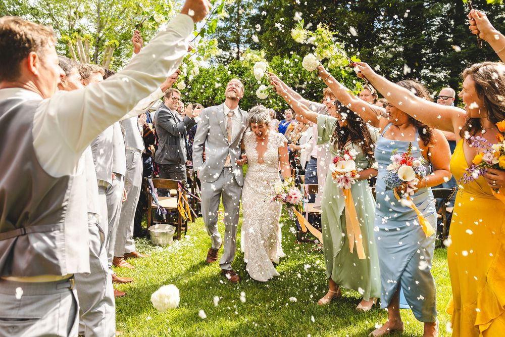 Bride and groom walk through confetti shower thrown by wedding guests during outdoor ceremony exit.
